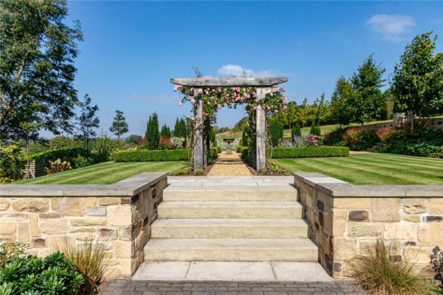 Well maintained garden with stairs up to a lawned area through a pergola